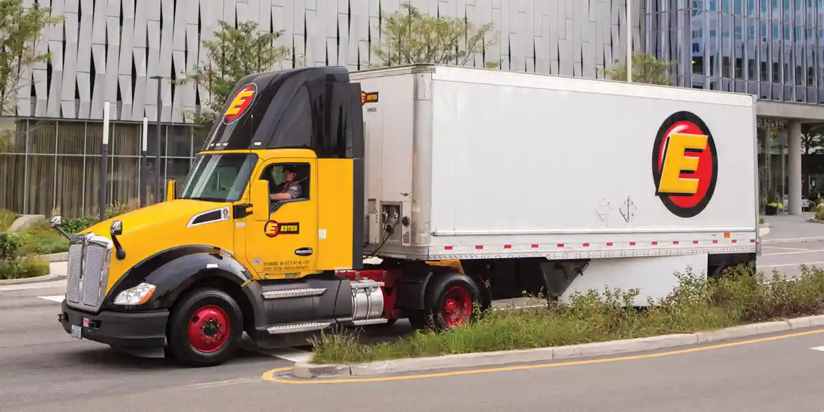 Picture of an Estes Truck on the road in front of buildings.